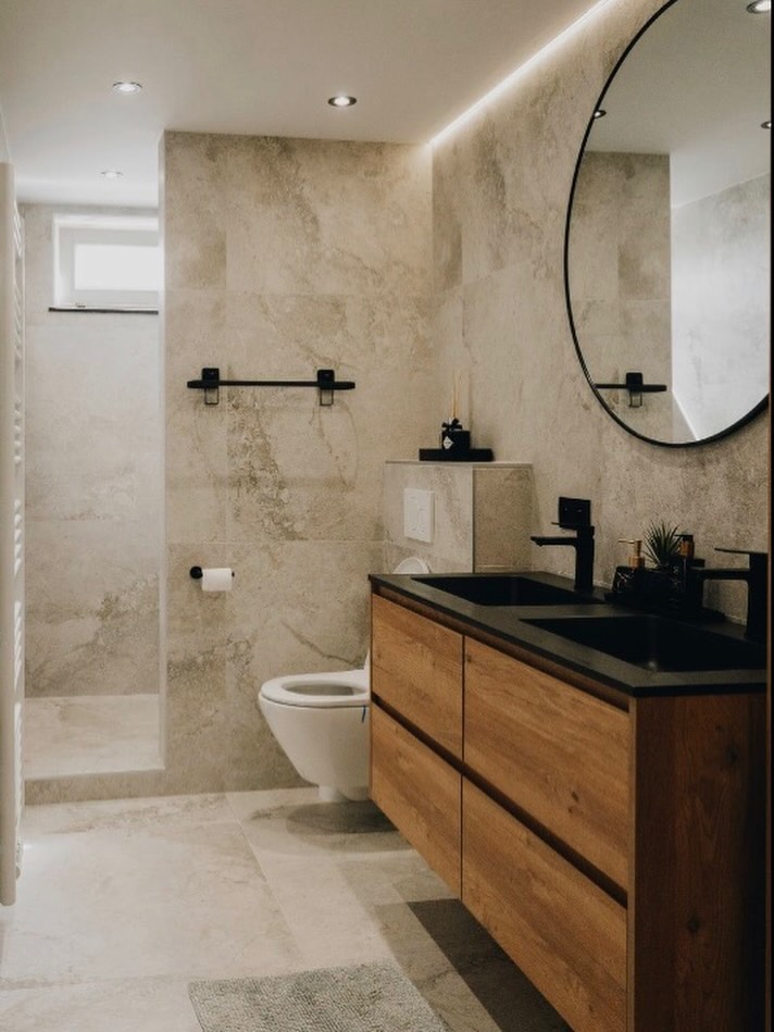 Baño reformado con revestimiento de piedra, mueble de madera y grifería negra