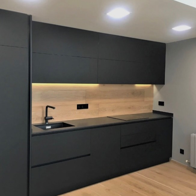 Cocina reformada con muebles negros mate y frente de madera iluminado